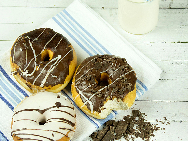 Delicious assortment of chocolate and vanilla glazed donuts on a striped cloth, accompanied by a refreshing glass of milk.