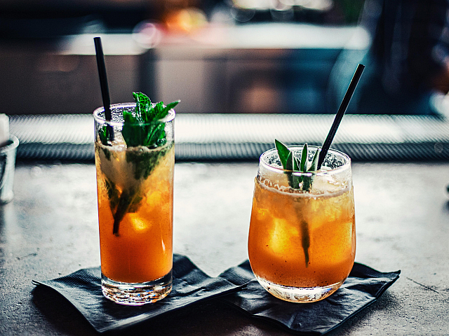 Vibrant pair of sunset-orange cocktails adorned with fresh mint and served elegantly on a sleek dark counter, perfect for a refreshing evening.