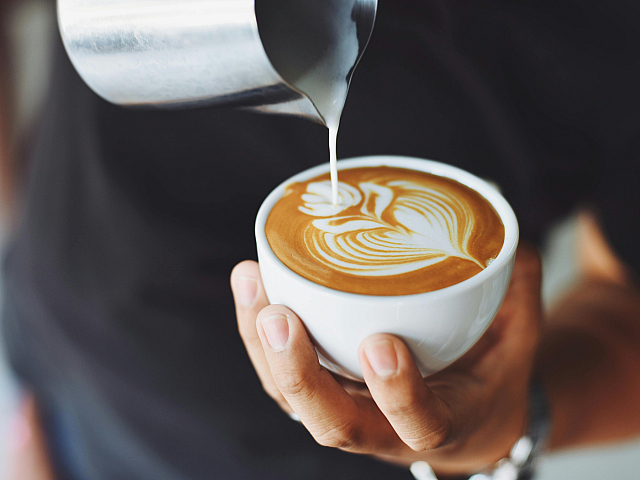 Artisan barista crafting intricate latte art with creamy milk in a ceramic cup.