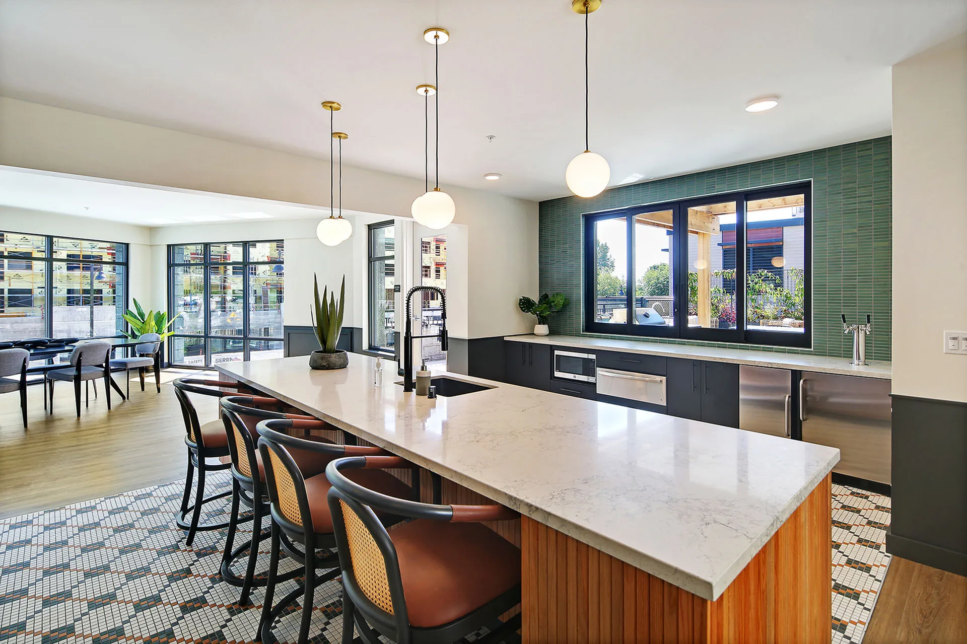 Modern community kitchen with a sleek marble island, stylish pendant lighting, and elegant seating, offering ample natural light and lush outdoor views.