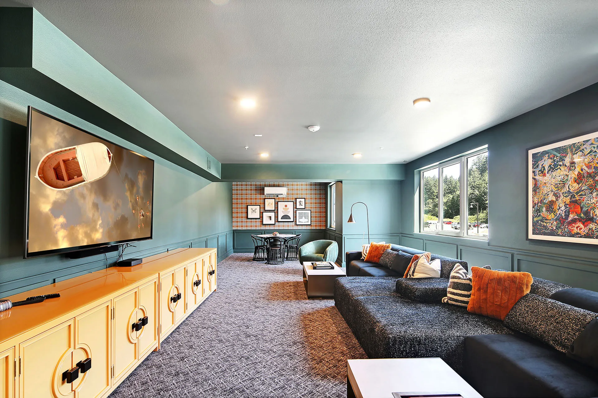 Luxurious living room with modern decor, featuring a large flat-screen TV, stylish yellow cabinet, comfortable sectional sofa with vibrant cushions, and abundant natural light from expansive windows.