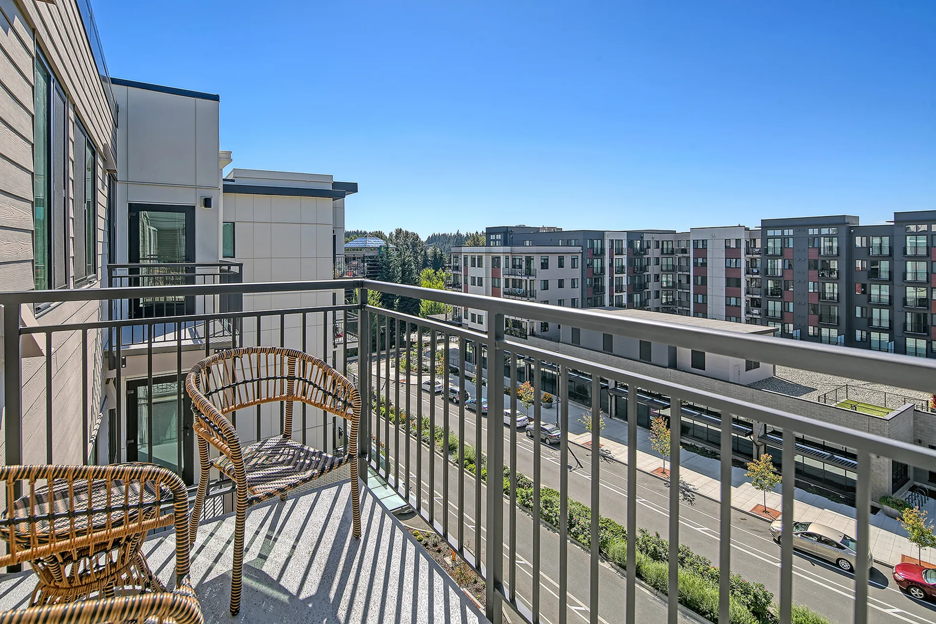 Chic balcony with modern wicker chairs overlooking a vibrant urban landscape and contemporary apartments under a clear blue sky.