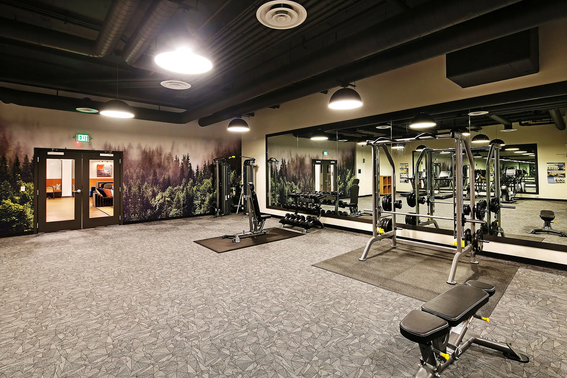 Modern fitness center featuring sleek workout equipment and an inspiring forest mural backdrop.