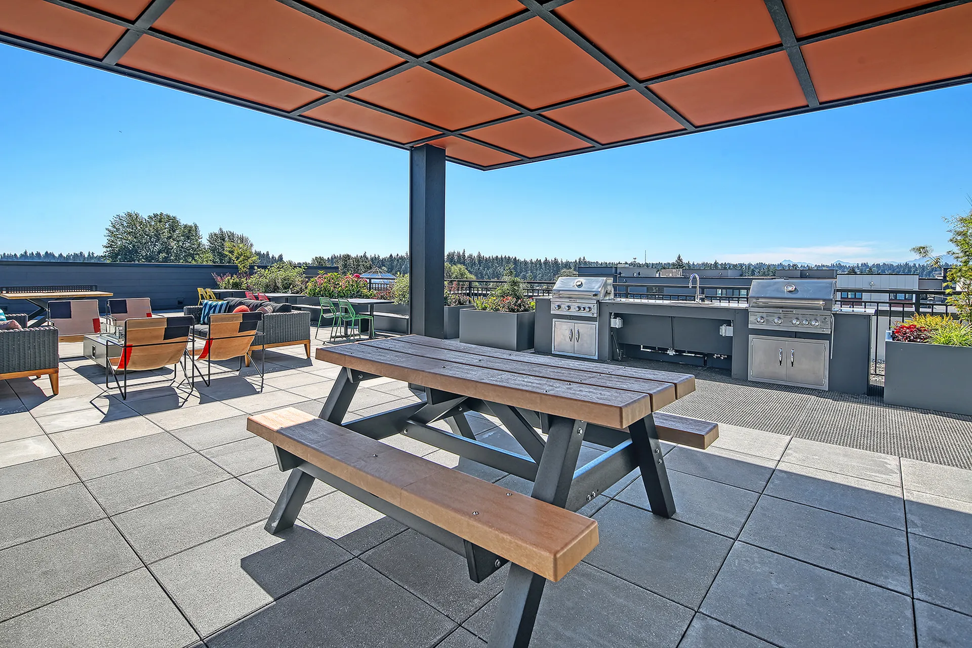 Elegant rooftop terrace with modern outdoor seating, a picnic table under a stylish canopy, and a state-of-the-art grill area, offering scenic views.