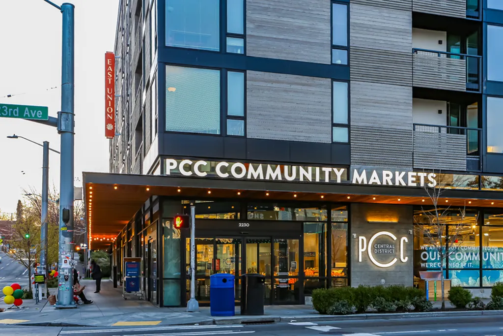 Modern urban apartment building with a ground-floor PCC Community Market, located at a bustling street corner at 23rd Ave and East Union.