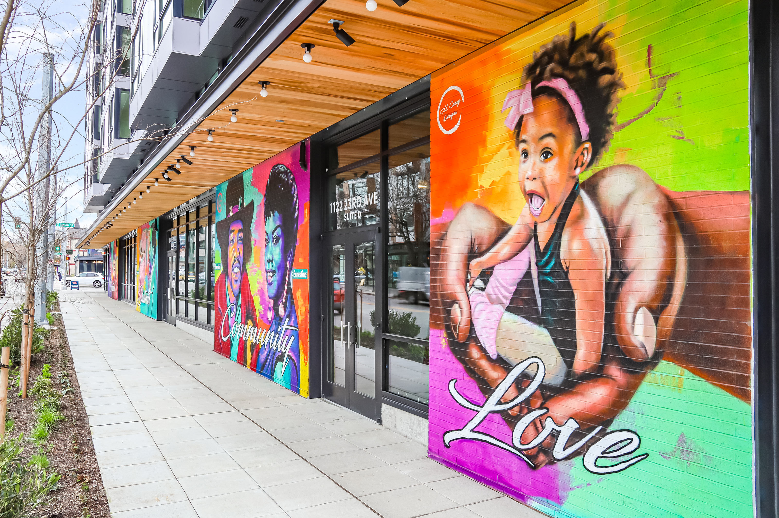 Vibrant street mural showcasing colorful portraits and the words \'Community\' and \'Love\' on a modern building facade, enhancing the urban environment.