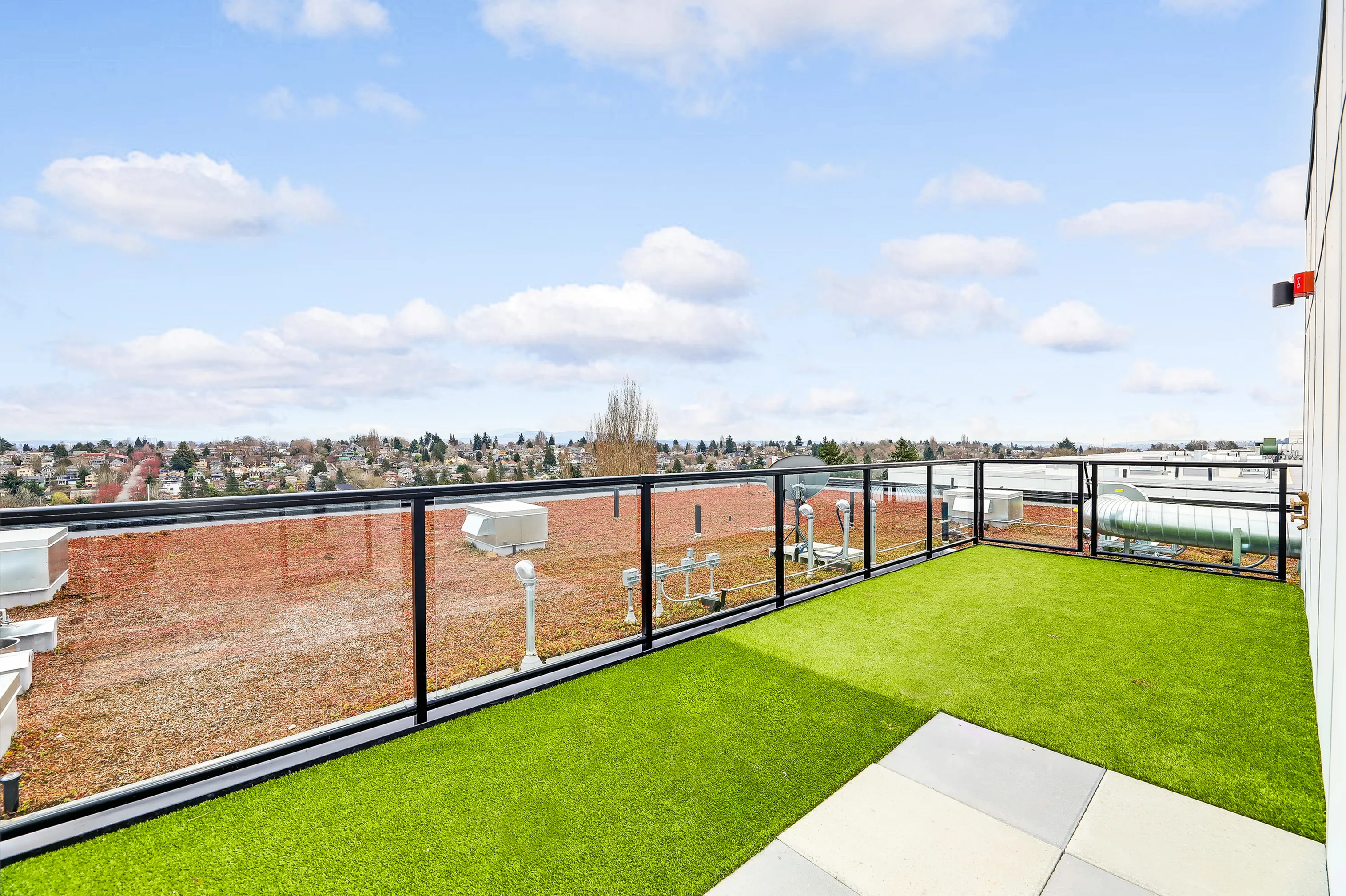 Spacious rooftop terrace with stunning city views, vibrant artificial grass, and sleek glass railings.