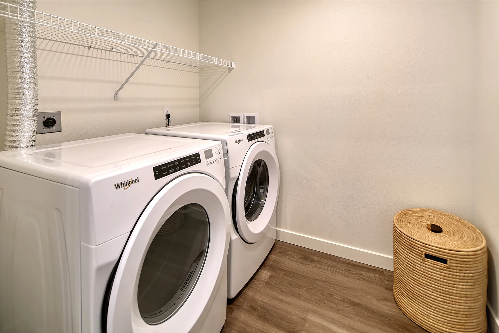 Modern laundry room with sleek front-loading washer and dryer, light wood flooring, and convenient wicker laundry basket.