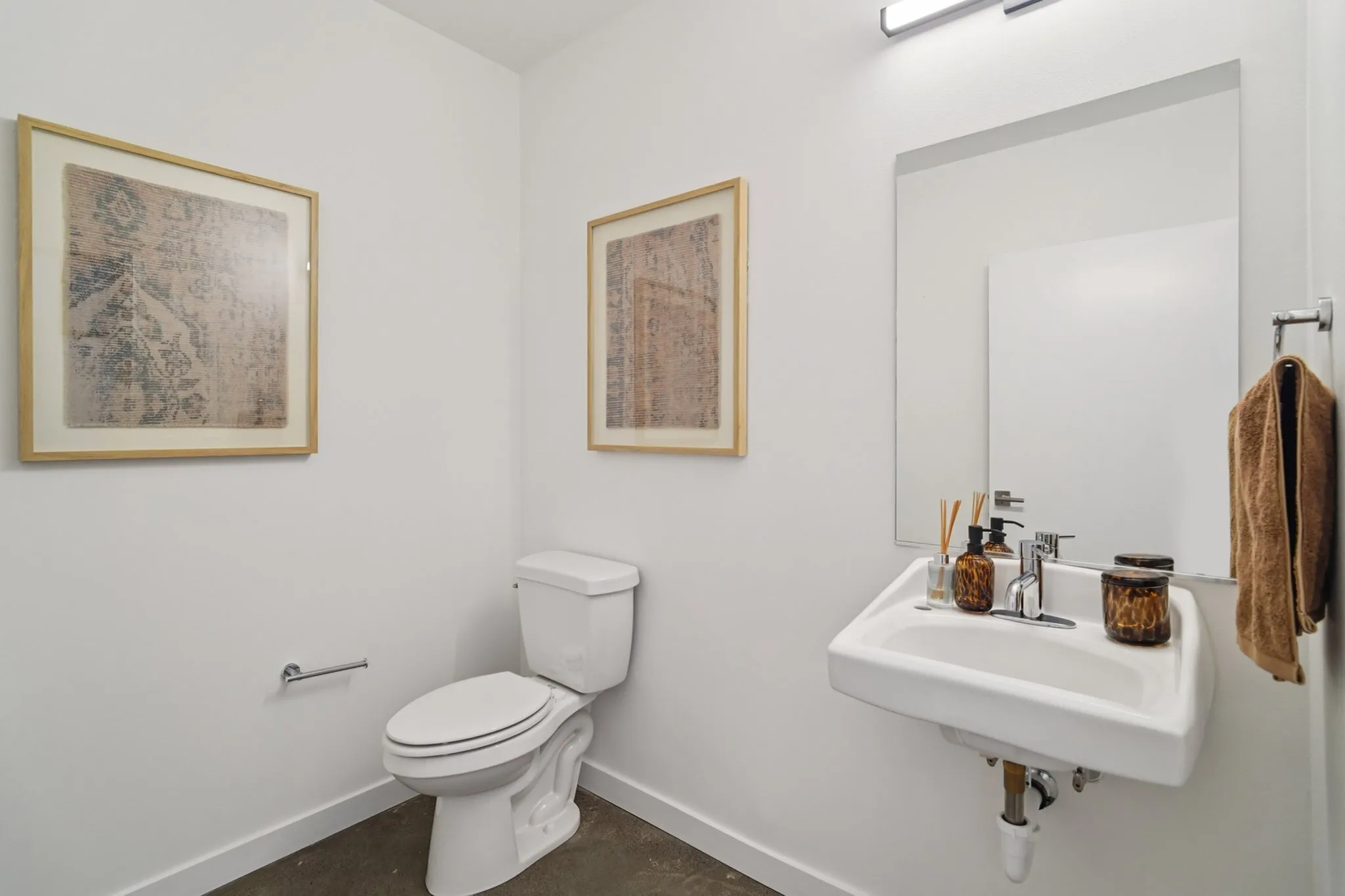 Elegant minimalist bathroom featuring a sleek white toilet and sink, wall-mounted with contemporary decor and framed artwork.