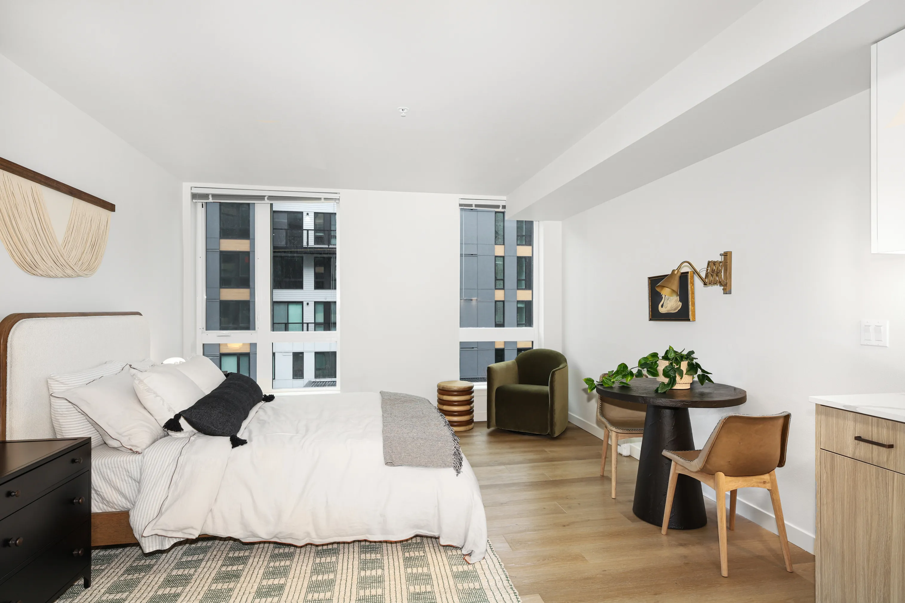 Bright and modern bedroom with stylish decor, featuring a cozy bed, sleek black dresser, and a charming seating area by large windows.