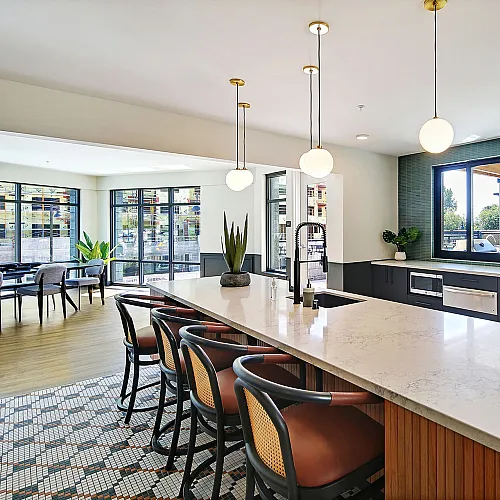 Bright and modern kitchen with elegant pendant lighting, marble countertops, and sleek cabinetry, overlooking a scenic view through large windows.