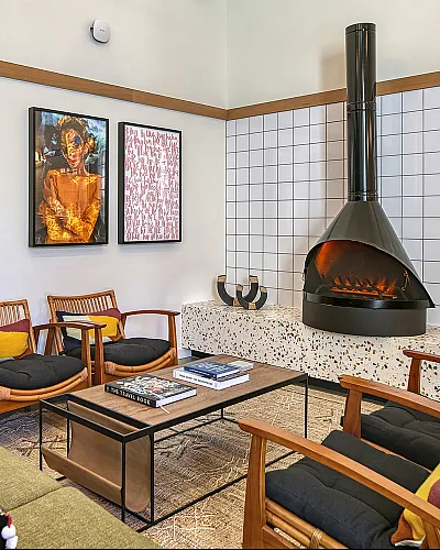 Chic living room featuring a stylish black fireplace, vibrant artwork, and elegant wooden seating with colorful cushions.