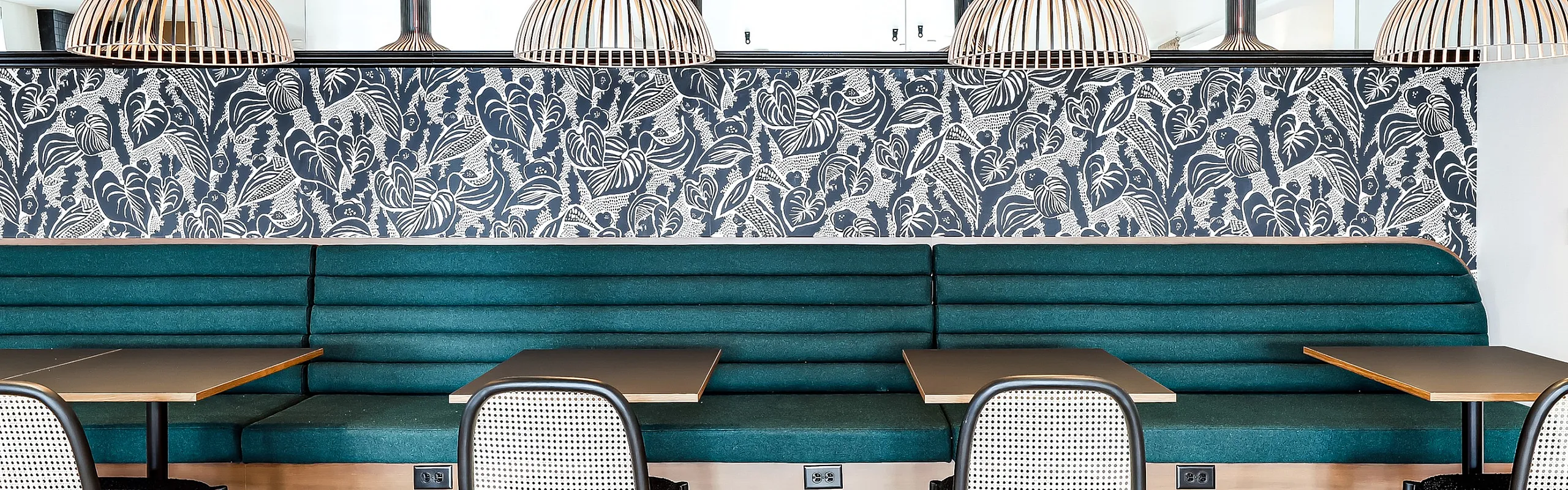 Elegant dining area with chic pendant lights, modern teal seating, and vibrant patterned wallpaper, creating a stylish ambiance.