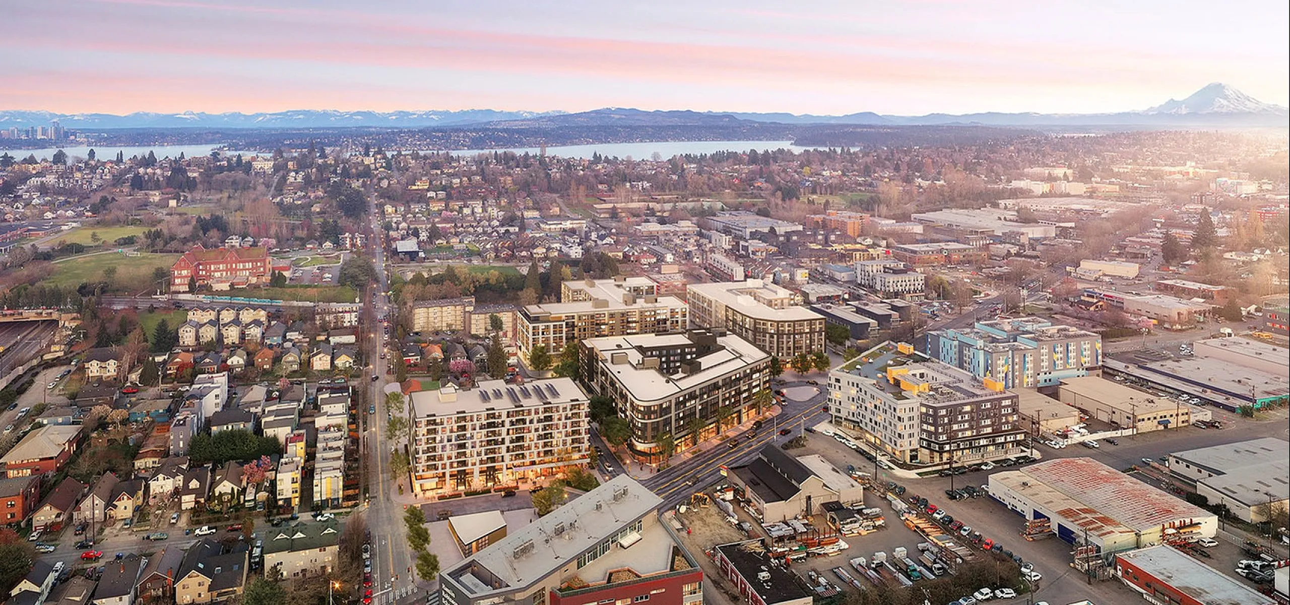 Beautiful aerial view of a vibrant urban neighborhood with modern apartments, lush greenery, and stunning mountain backdrop at sunrise.