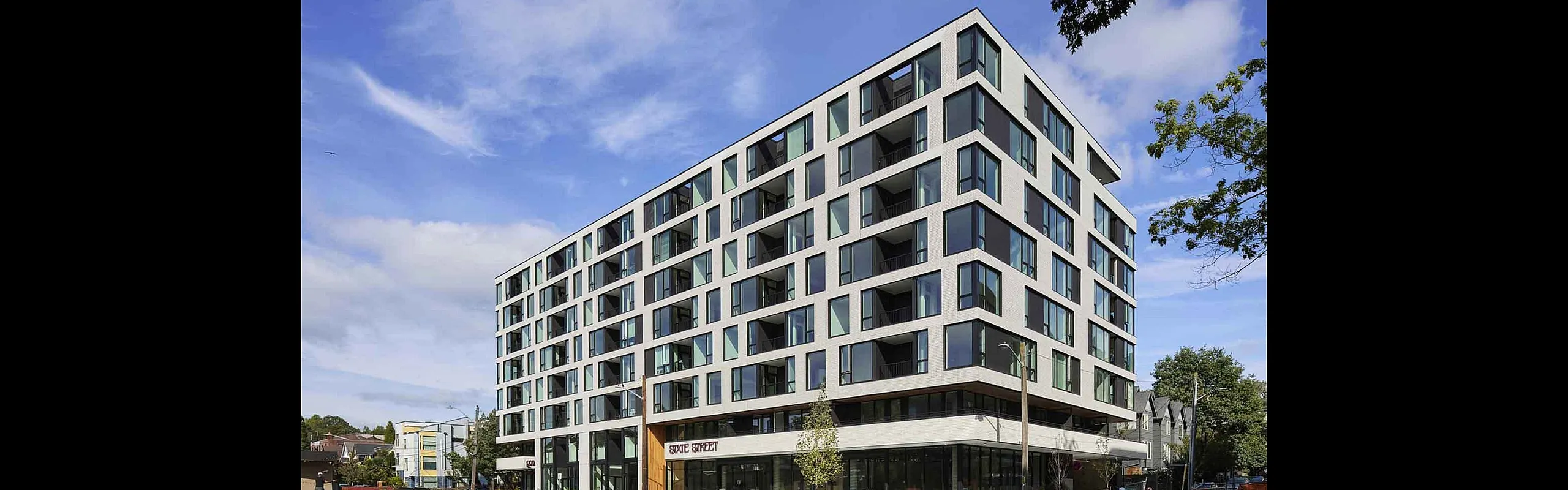 Contemporary six-story apartment building with sleek large windows and a modern facade in a vibrant urban setting.