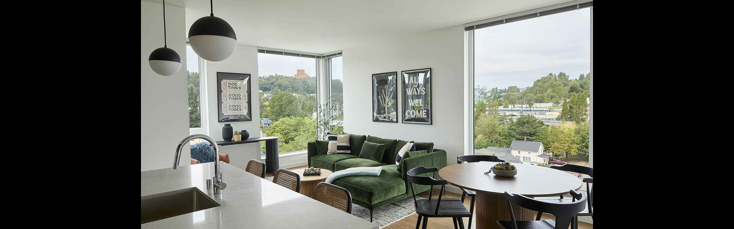 Modern apartment with an open-concept kitchen and living room featuring a chic green sofa, large windows with scenic views, and stylish decor.