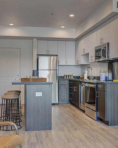 Modern kitchen with sleek cabinetry, stainless steel appliances, and a cozy breakfast bar, set against warm wooden flooring for a stylish living space.