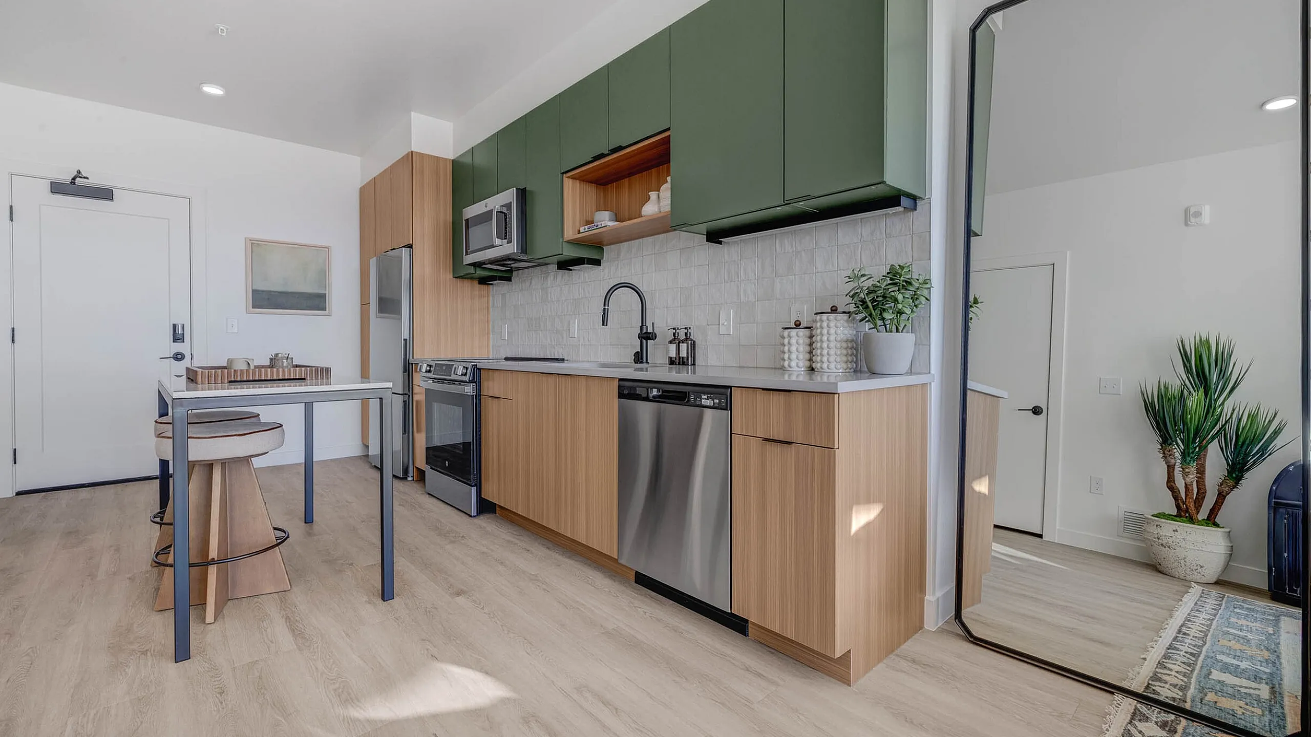 Modern kitchen with sleek green cabinets, stainless steel appliances, and elegant wood-finish accents, illuminated by natural light.