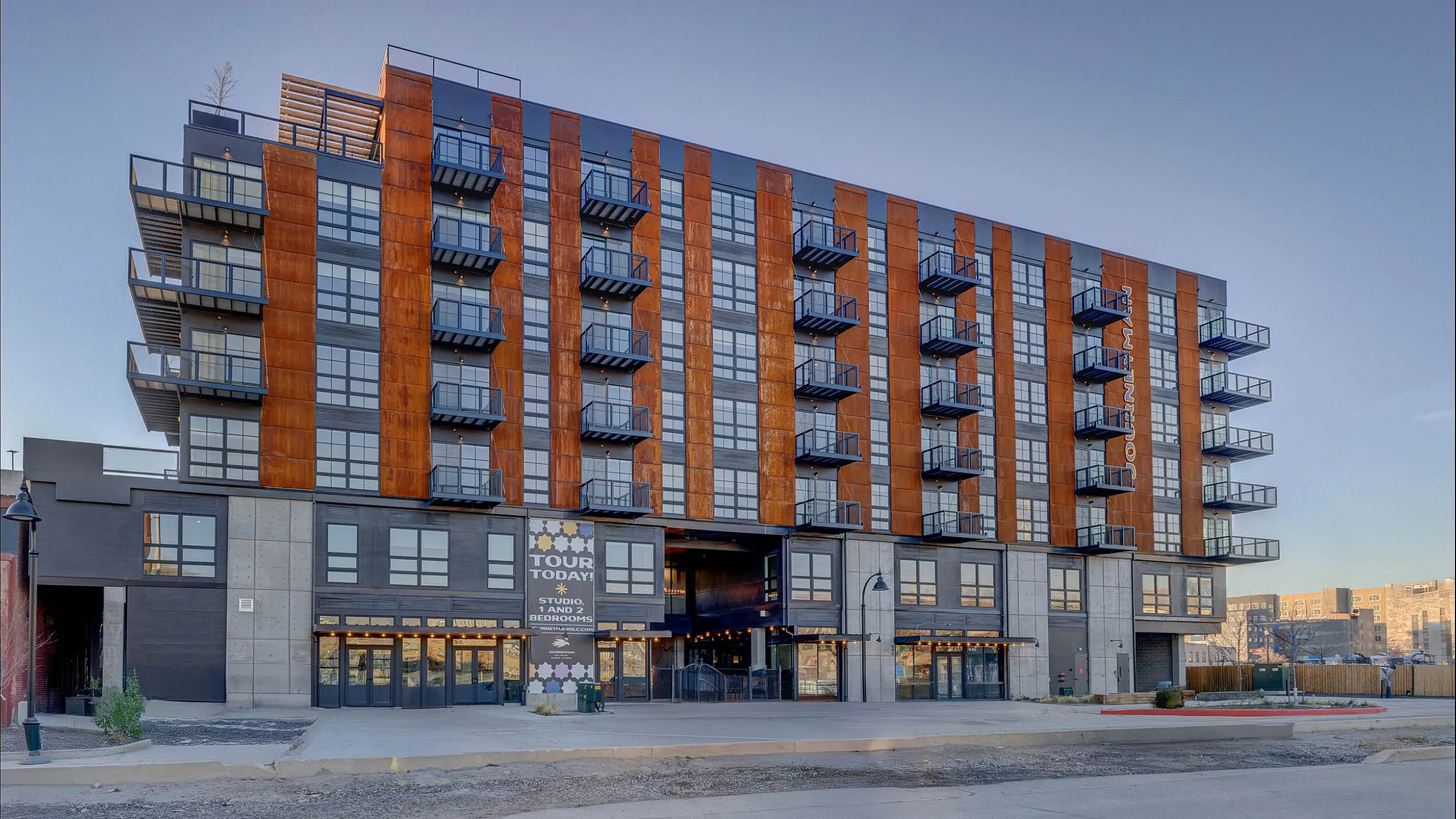 Contemporary apartment building with striking architectural design, featuring modern balconies and large glass windows, offering studio and 2-bedroom units for rent.