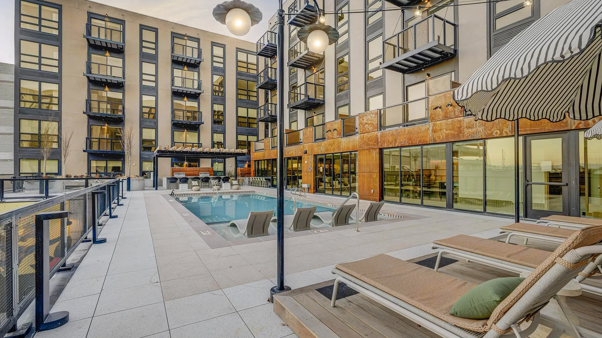 Modern apartment complex with a luxurious outdoor pool area, chic lounge chairs, and private balconies overlooking the sunset.