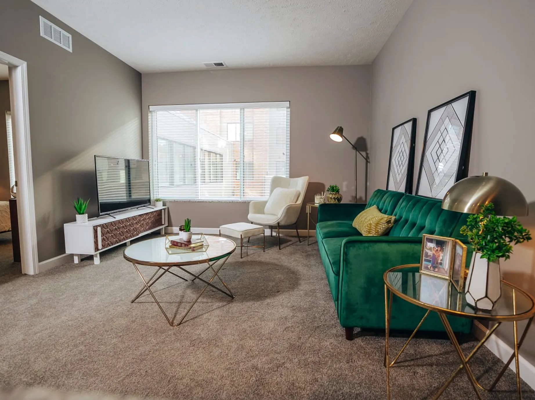 Chic modern living room with plush emerald sofa, stylish armchair, elegant decor, and a large window bathing the space in natural light.