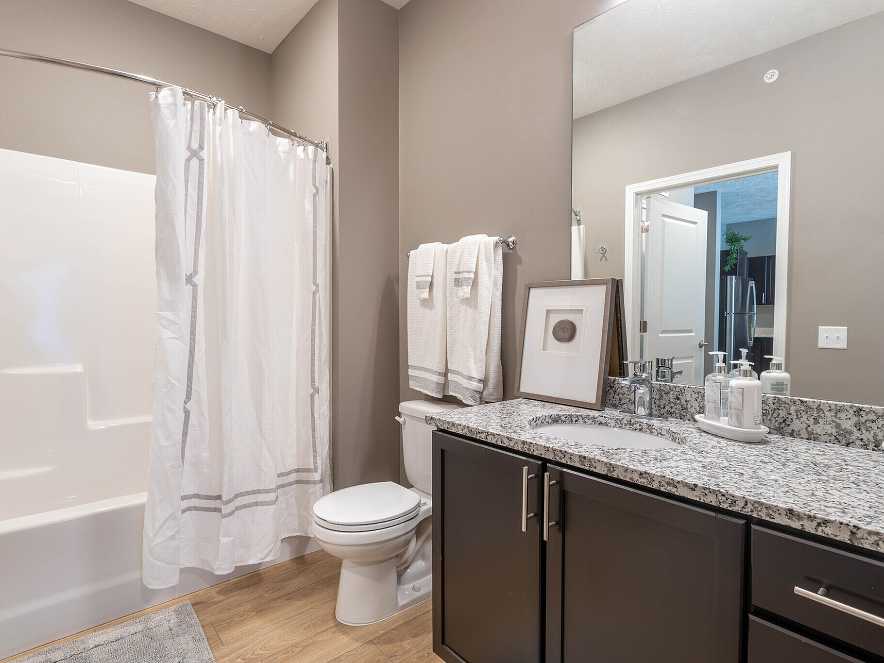 Modern bathroom with elegant granite countertop, sleek dark wood cabinets, and a pristine shower curtain, exuding sophistication and style.