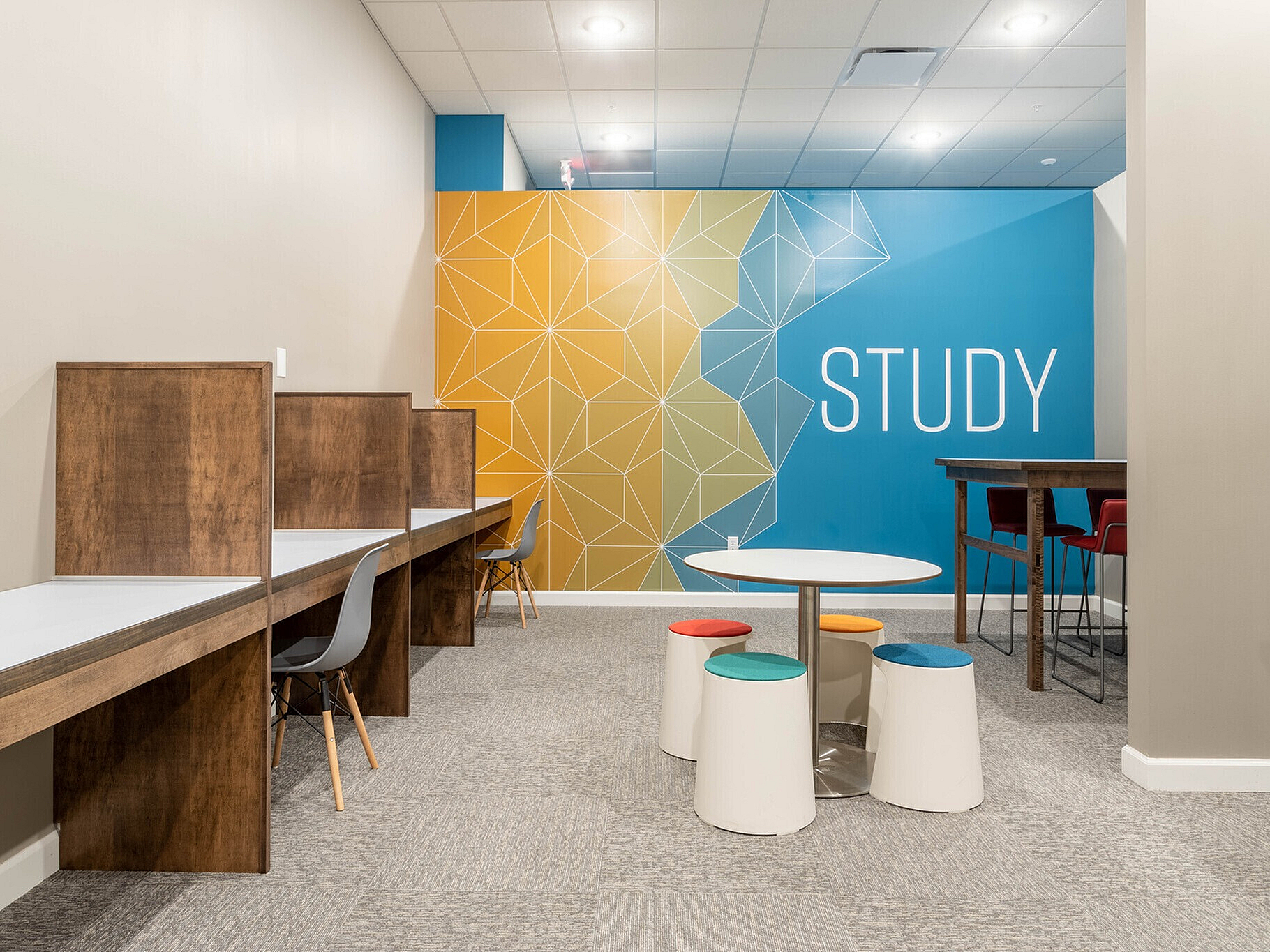 Modern study area with cozy wooden desks, vibrant geometric wall art, and colorful seating for a creative and productive environment.