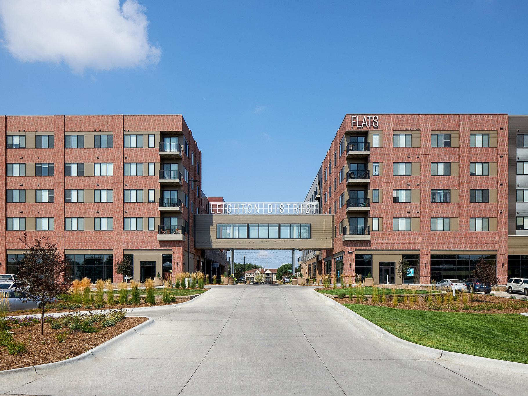 Modern apartment complex with stylish brick facade at Leighton District, featuring ample parking and vibrant landscaping, under a clear blue sky.