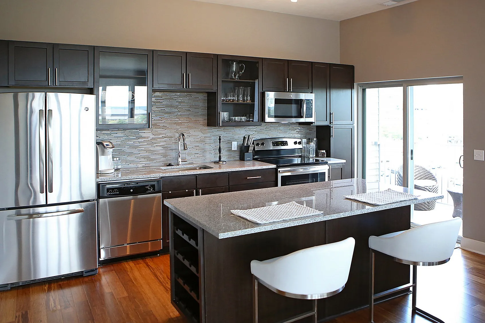 Modern kitchen with sleek stainless steel appliances, elegant cabinetry, and a spacious island featuring stylish bar seating, bathed in natural light from large sliding doors.