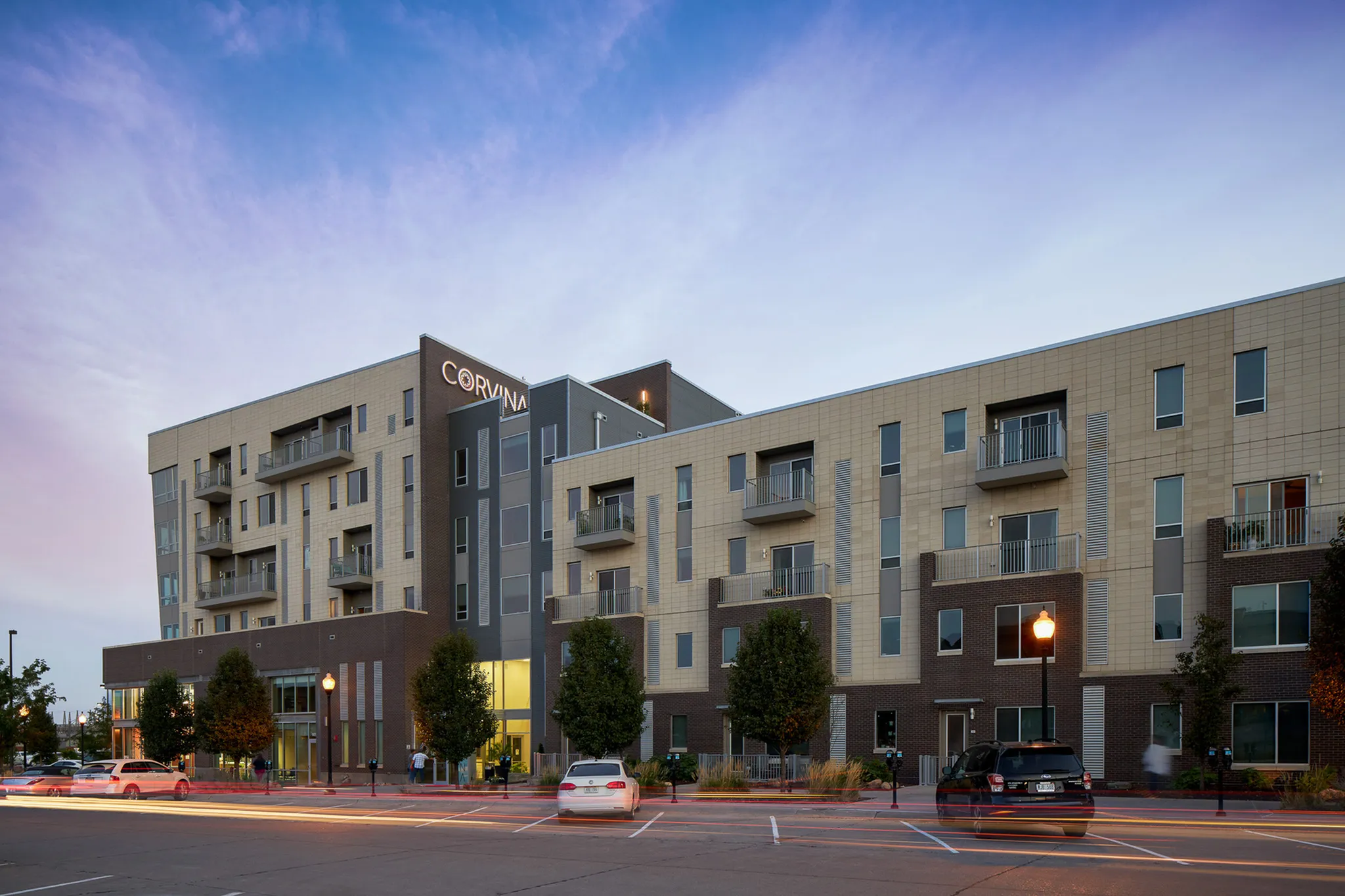 Modern apartment building with multiple balconies, contemporary facade, and warmly lit entrance at dusk.