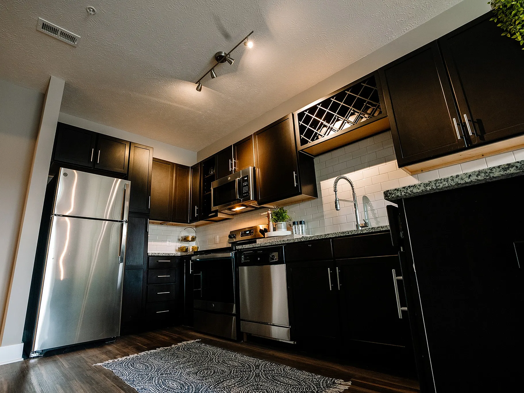 Modern kitchen with dark wood cabinets, stainless steel appliances, and elegant pendant lighting.