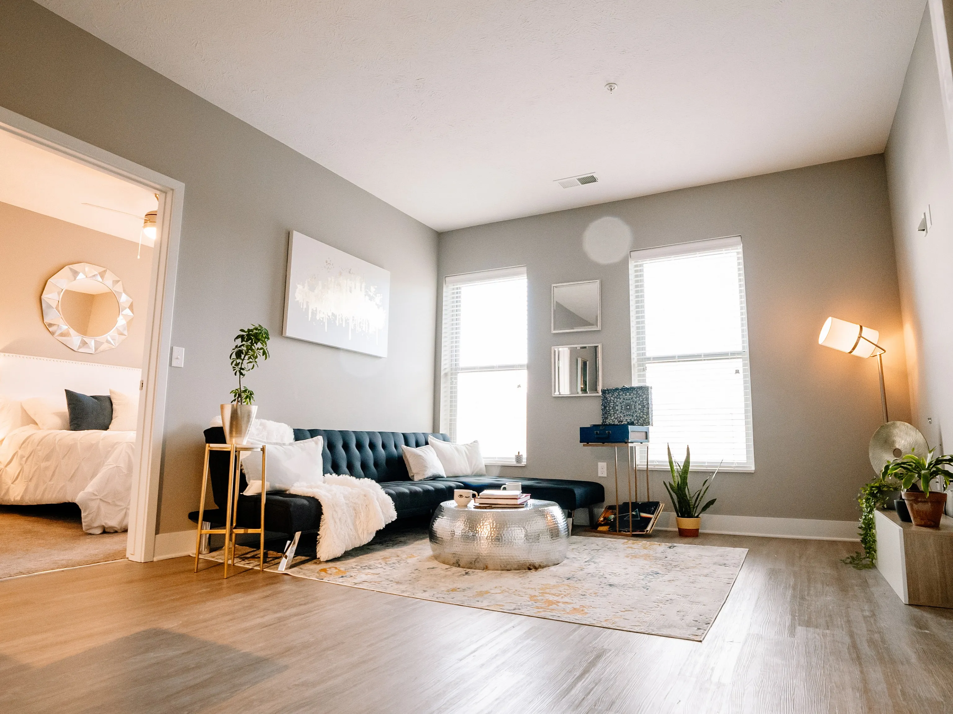 Chic living room with modern decor, featuring a black sofa, stylish floor lamp, and a glimpse into a cozy bedroom.