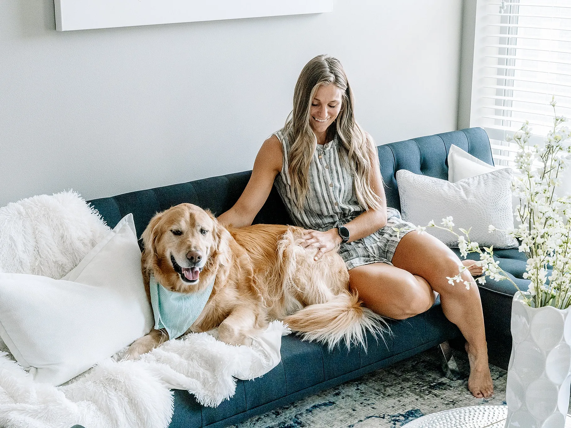 Bright and cozy living room with a woman relaxing on a stylish sofa, accompanied by a happy golden retriever and accented by elegant decor.