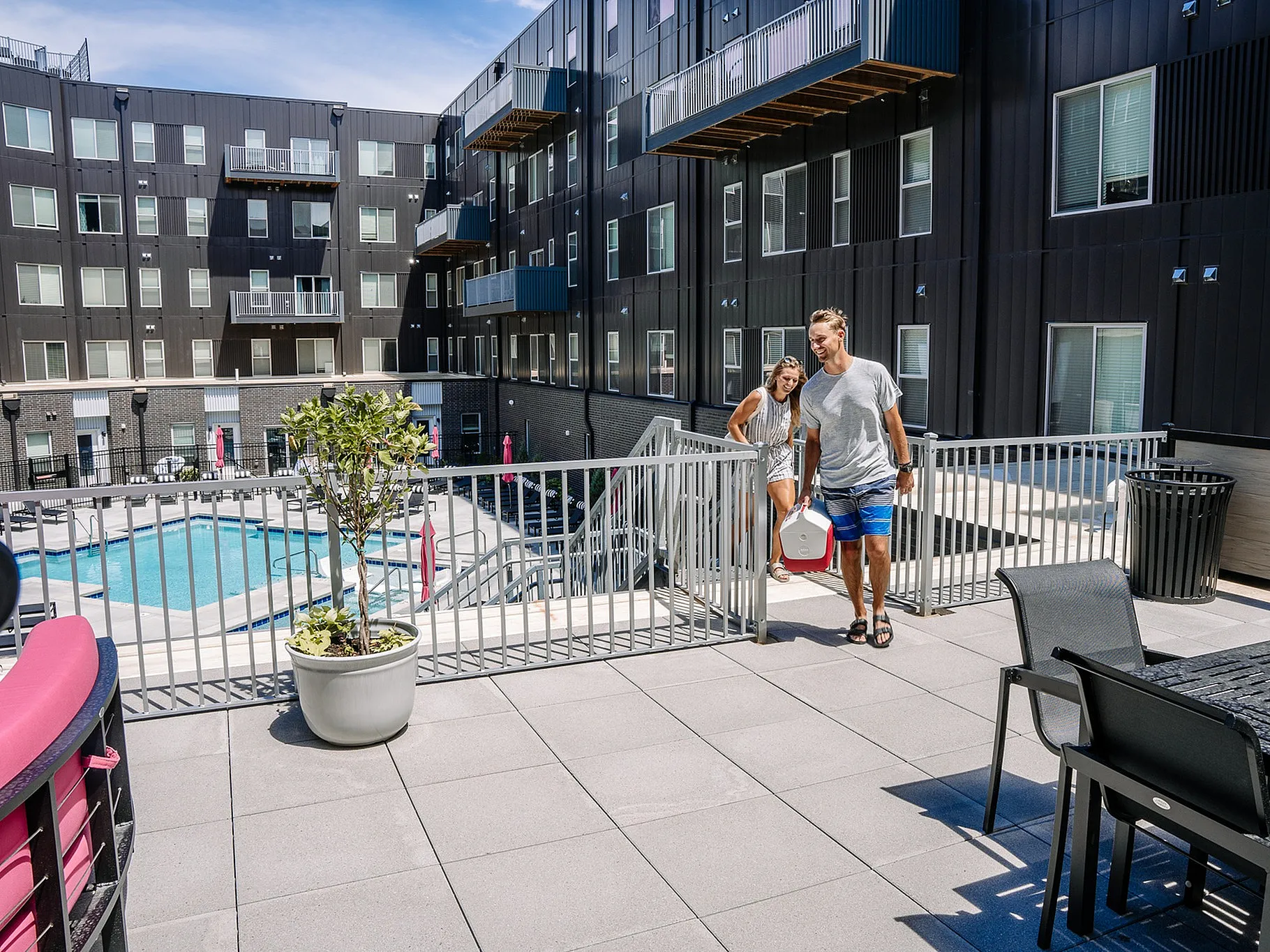 Modern apartment complex with spacious poolside terrace and stylish outdoor seating, perfect for leisure and relaxation.