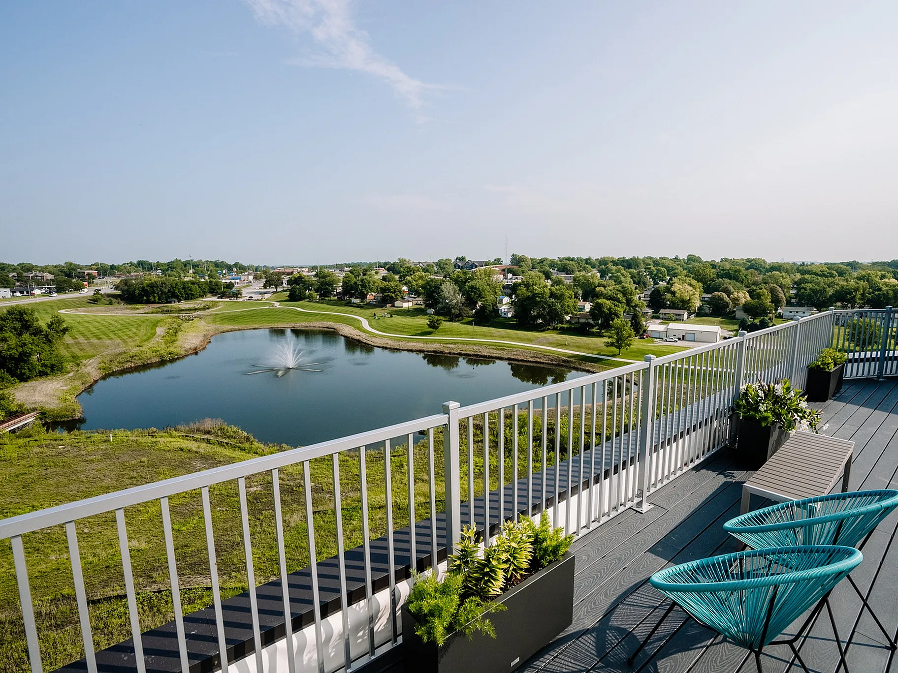 Expansive balcony with stunning views of a serene pond and lush green landscape, featuring modern outdoor seating and stylish plant arrangements.