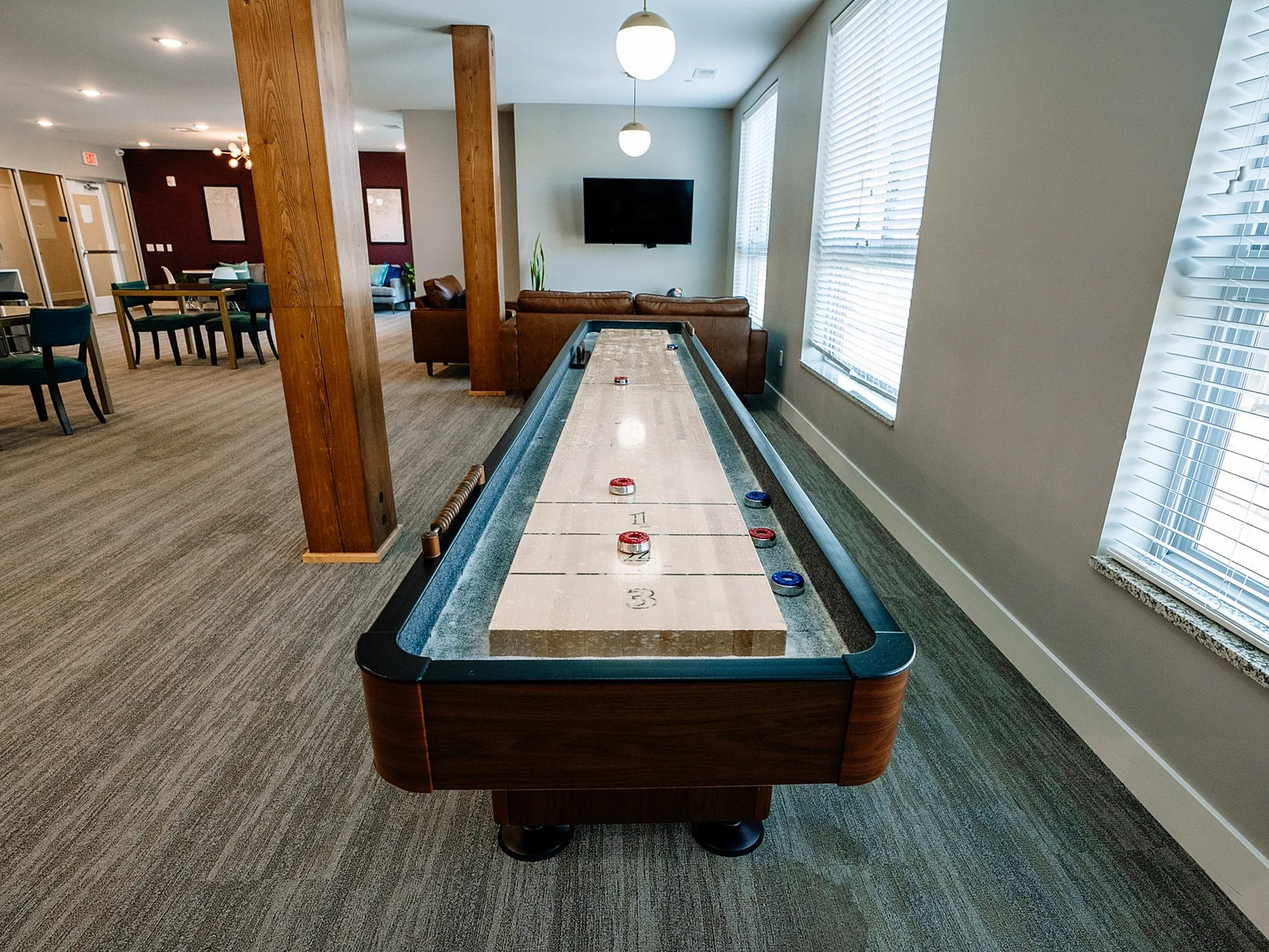 Chic apartment common room featuring a stylish shuffleboard table, modern seating, and large windows for natural light.