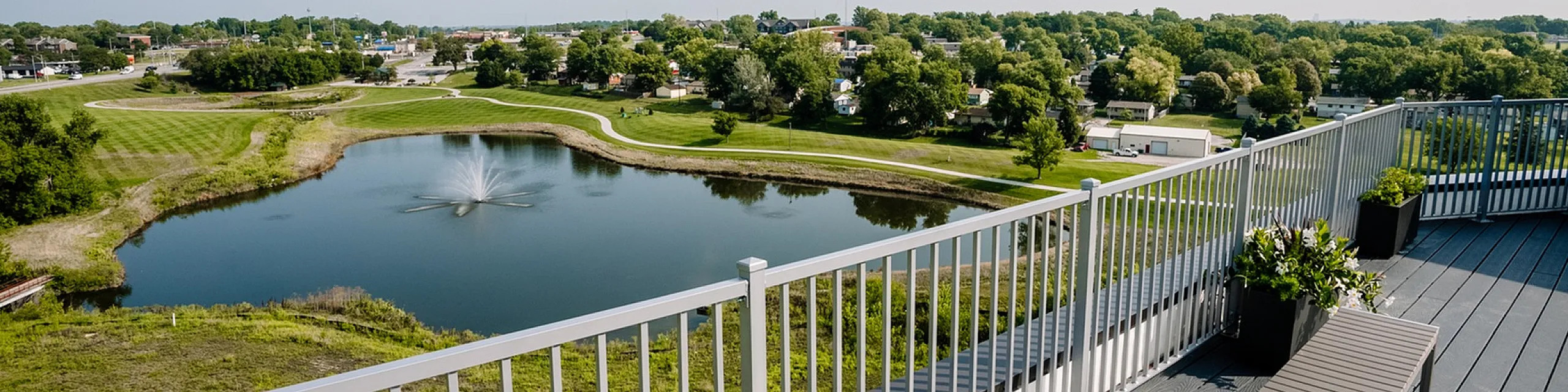 Stunning apartment balcony offering serene views over a landscaped pond with a fountain, lush greenery, and a spacious seating area for relaxation.