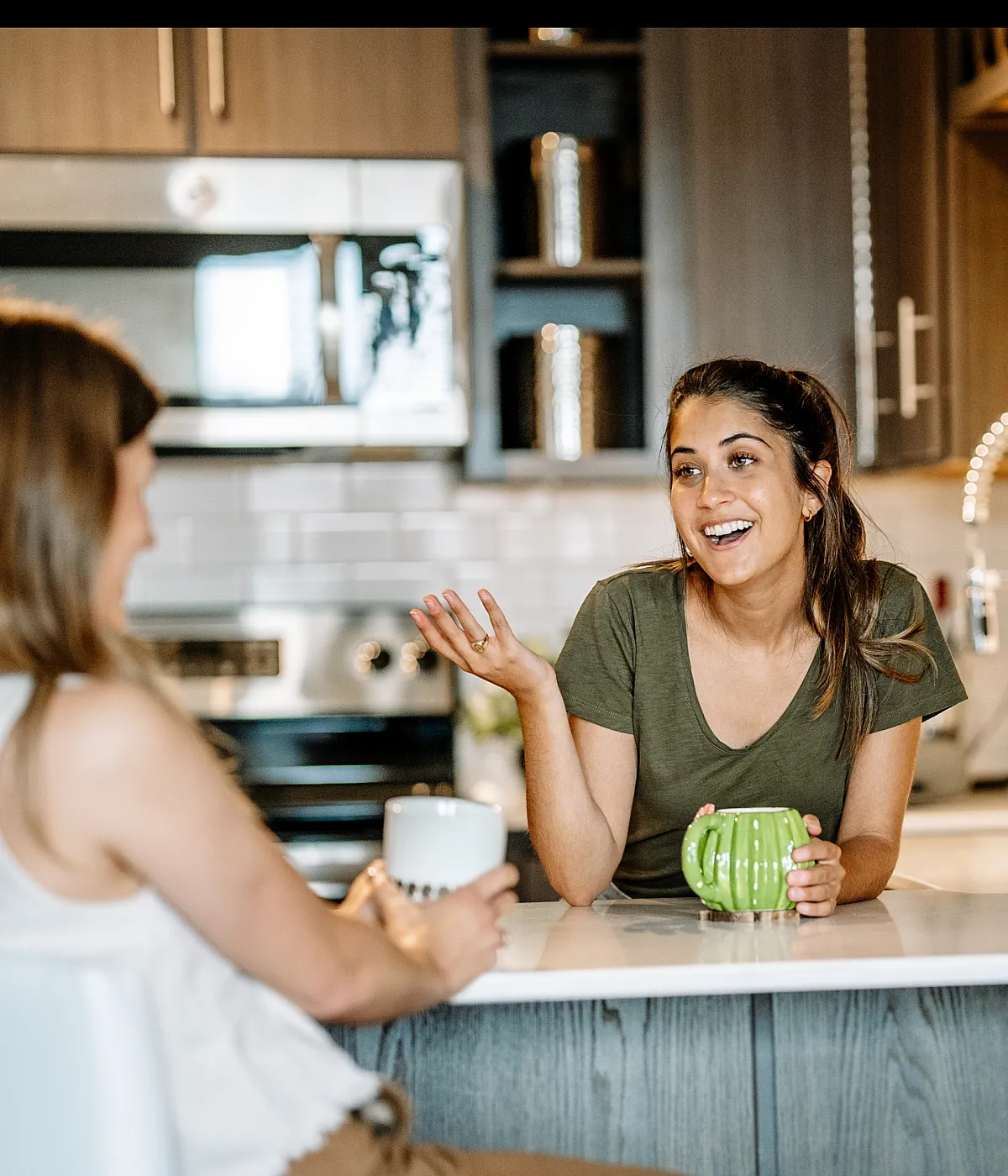 Modern kitchen with friends enjoying a chat over coffee at a stylish countertop, surrounded by sleek cabinetry and lush greenery.