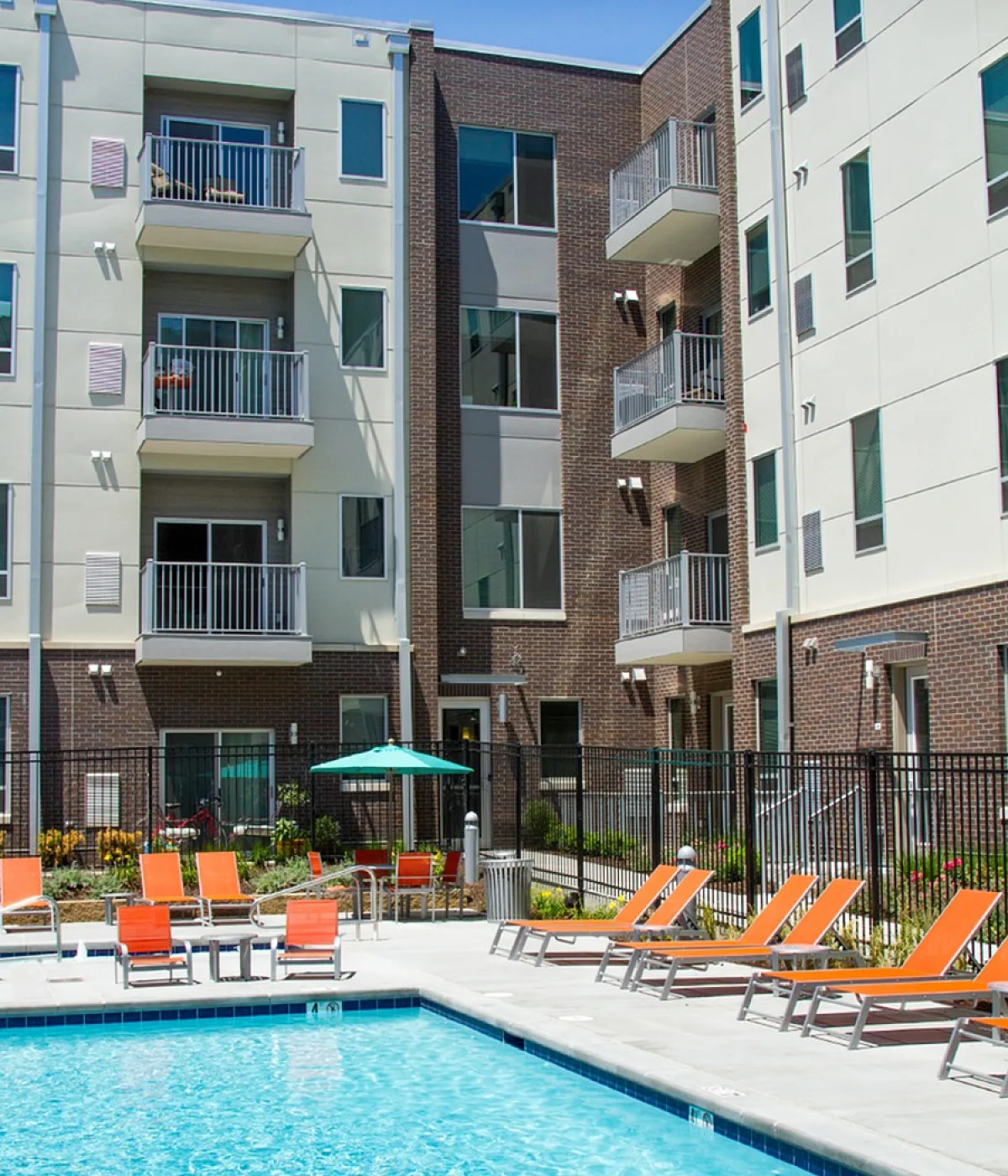Stunning apartment complex featuring a sparkling swimming pool with orange lounge chairs and modern balconies, perfect for relaxation and luxury living.