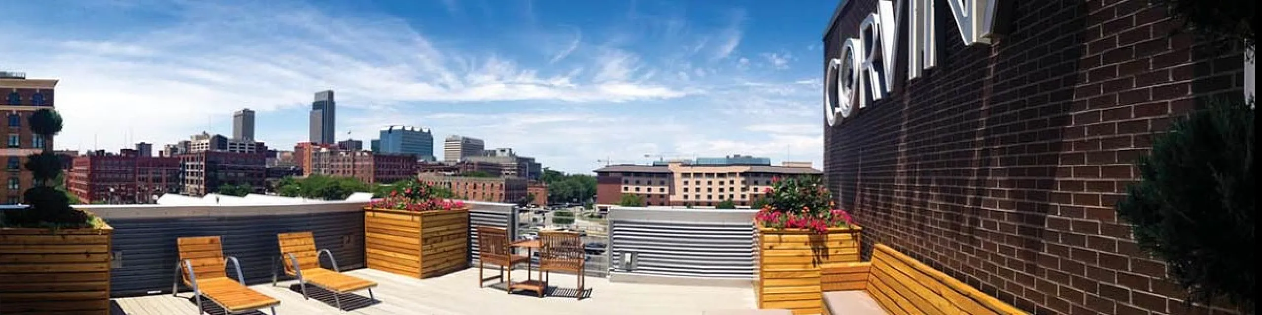 Luxurious rooftop terrace featuring stylish wooden lounge chairs and vibrant planters with panoramic city views.