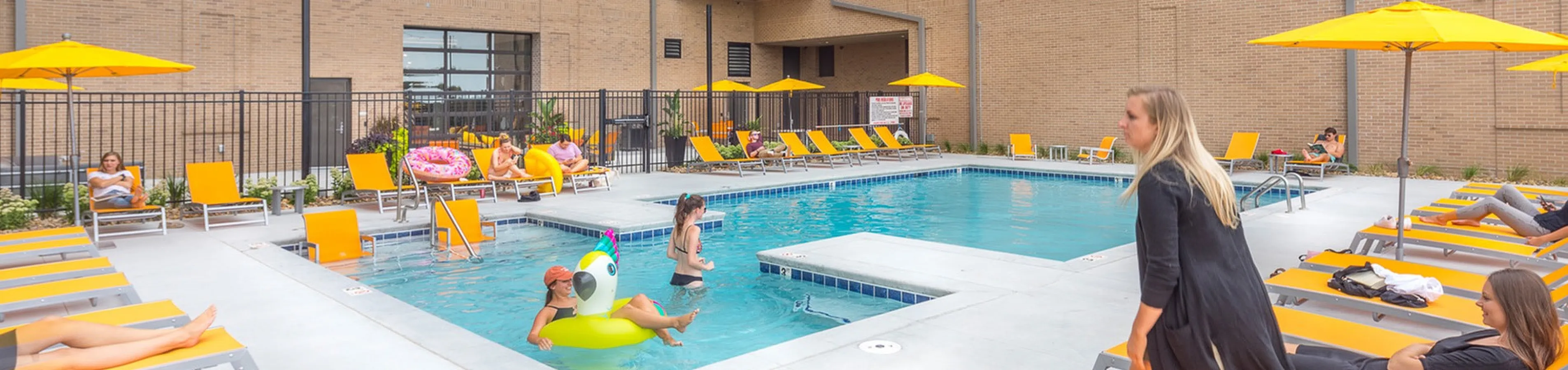 Vibrant urban apartment courtyard featuring a modern pool area with stylish yellow sun loungers and cheerful umbrellas.