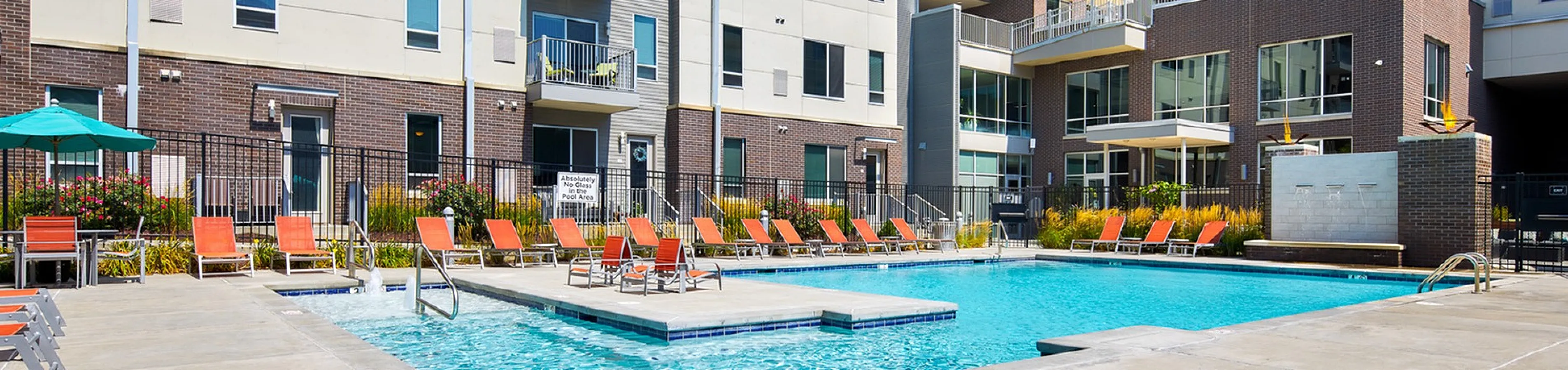 Modern apartment complex with a vibrant pool area and comfortable lounging chairs, perfect for relaxation and recreation.