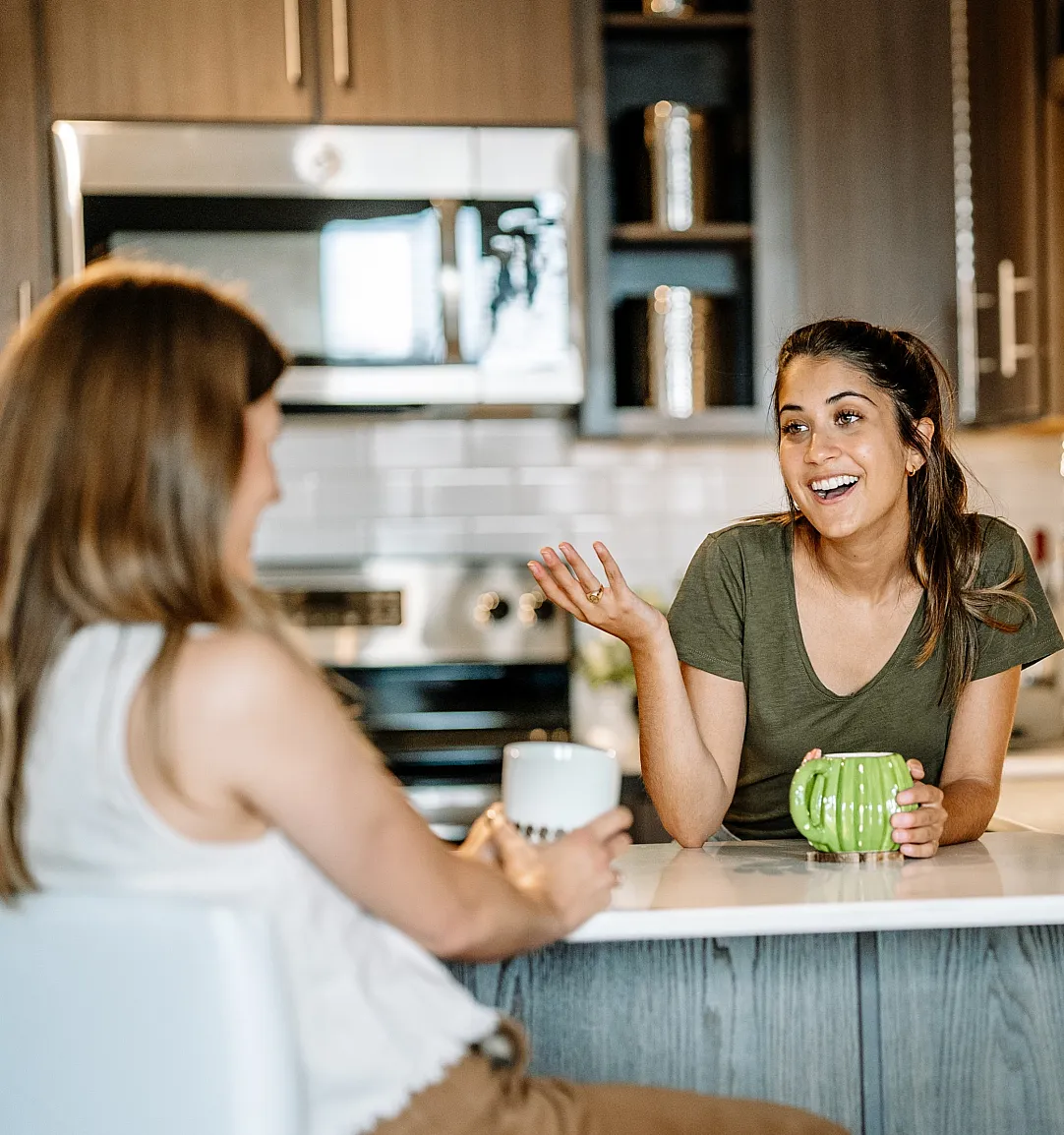 Modern kitchen setting with three individuals enjoying coffee, surrounded by sleek cabinetry, stainless steel appliances, and vibrant greenery.
