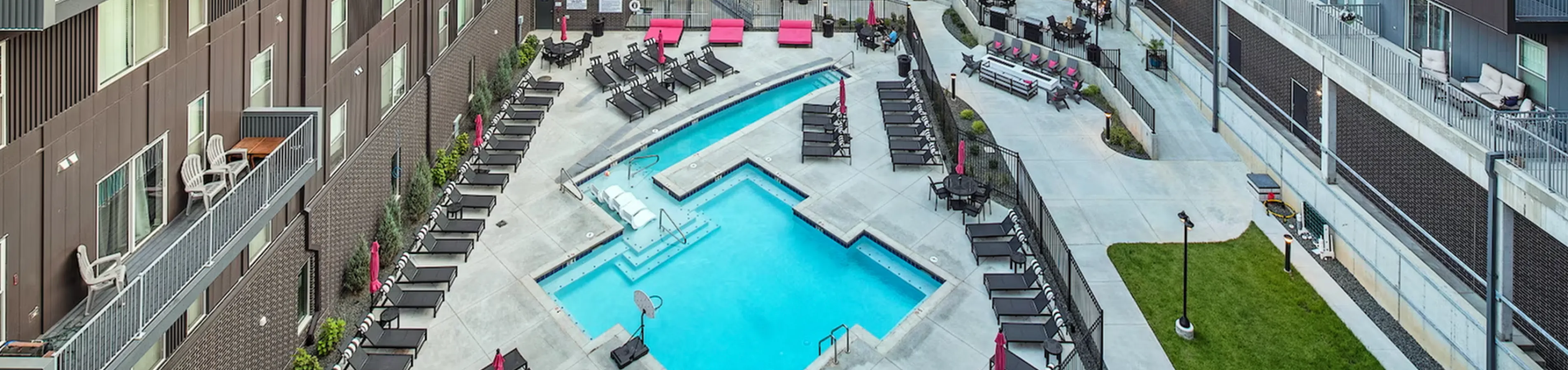 Modern apartment complex with a vibrant outdoor pool area, surrounded by stylish lounging chairs and balconies, offering luxury living.