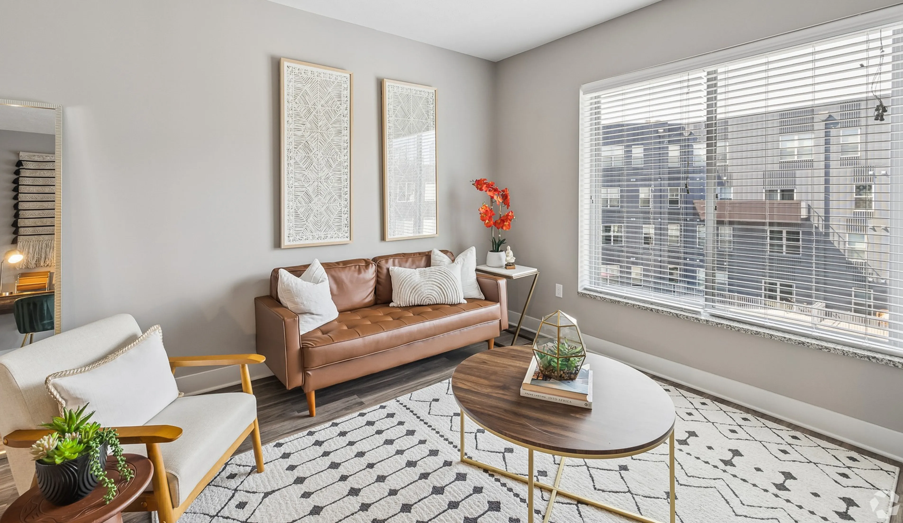 Bright and modern living room with stylish decor, featuring a cozy leather sofa, chic armchair, and large window allowing natural light to flood the space.