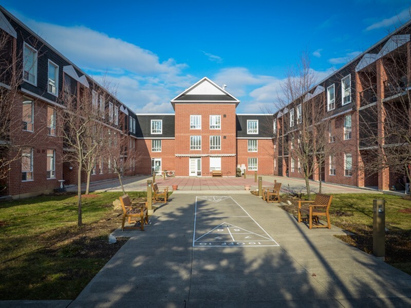 Charming brick apartment complex with a welcoming courtyard and outdoor seating, under a bright blue sky.
