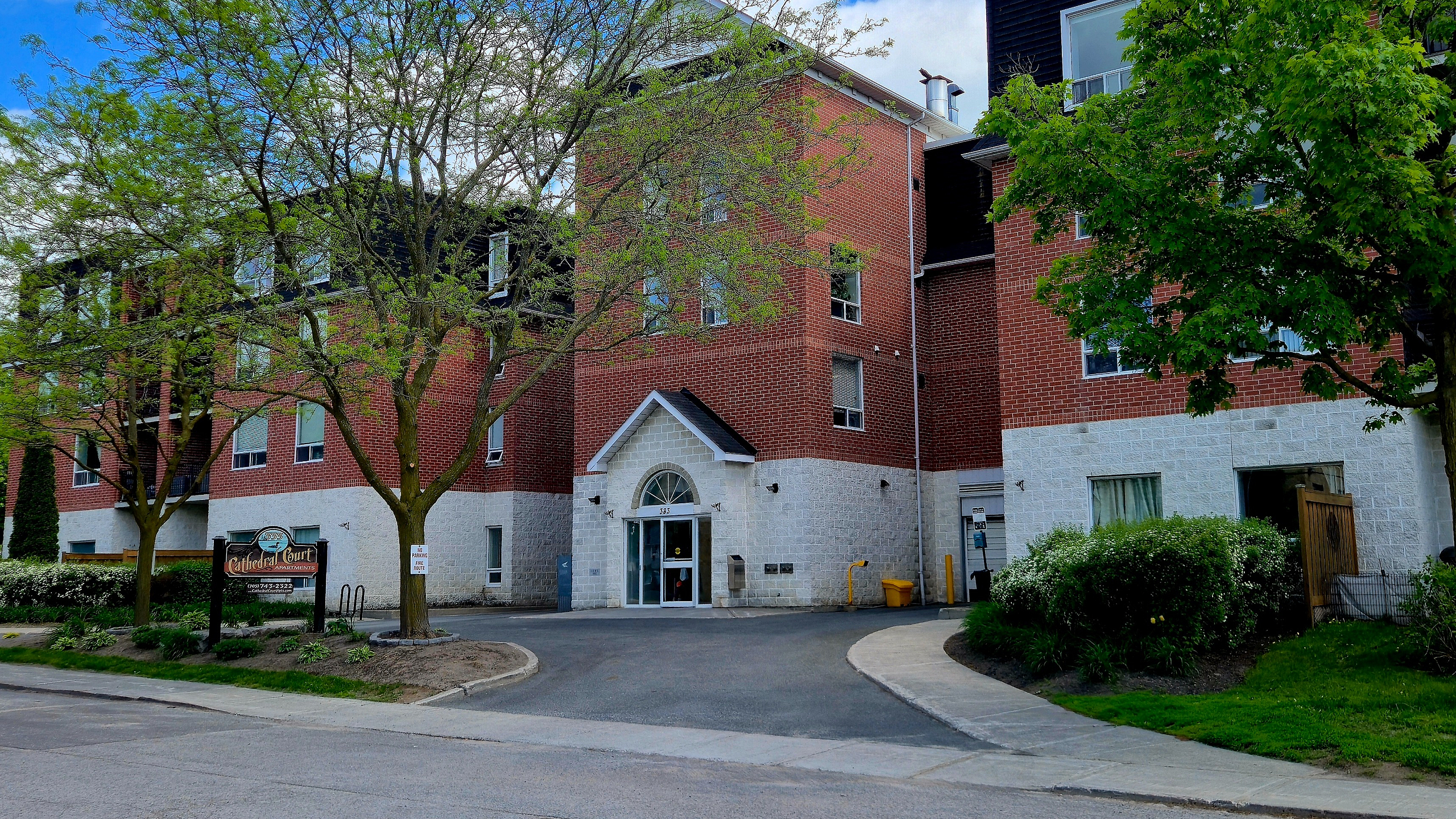 Charming red-brick apartment building surrounded by lush green trees, offering a serene and inviting atmosphere.