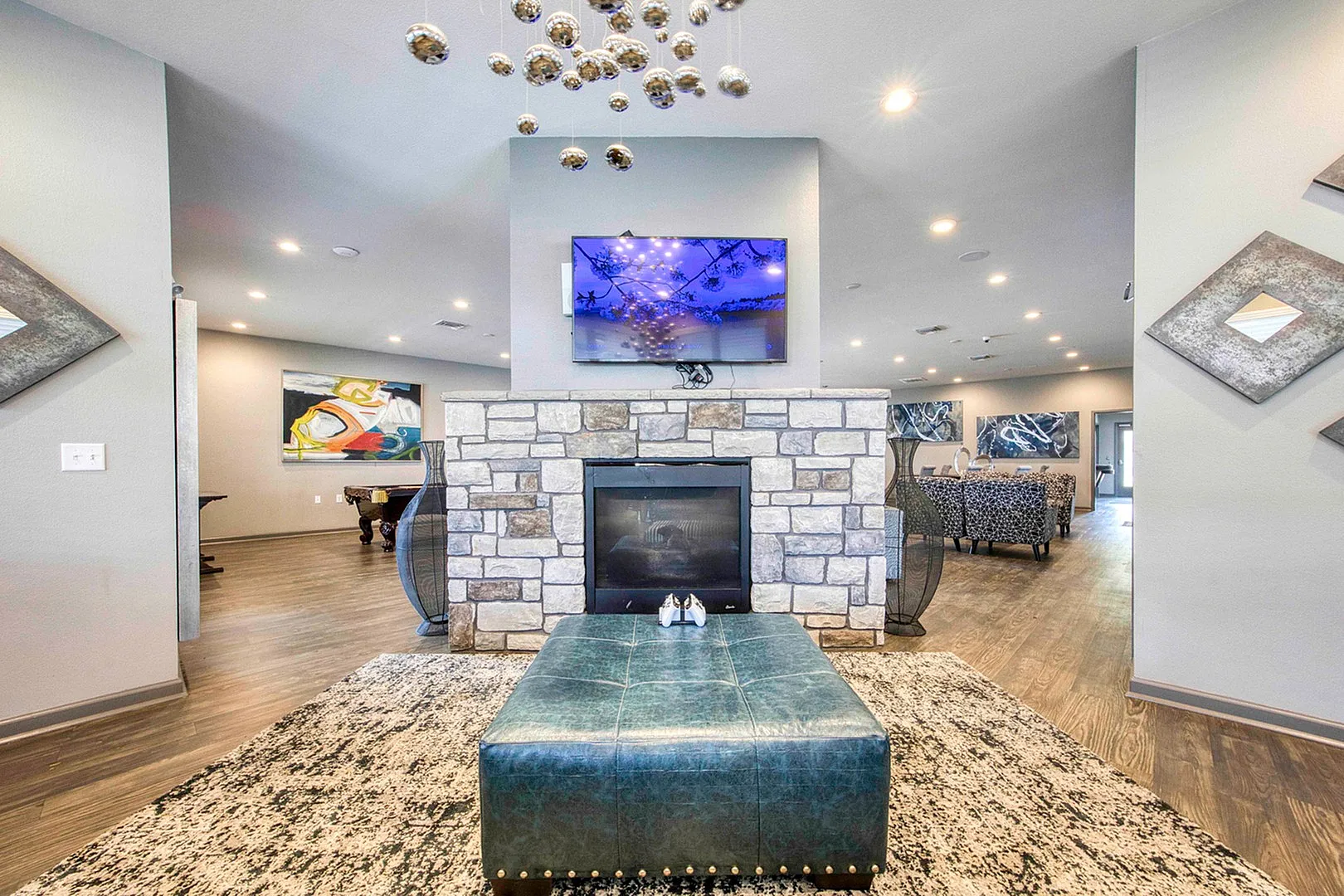 Elegant living space with a modern stone fireplace, stylish ottoman, and chic decor, enhanced by vibrant art and soft lighting.