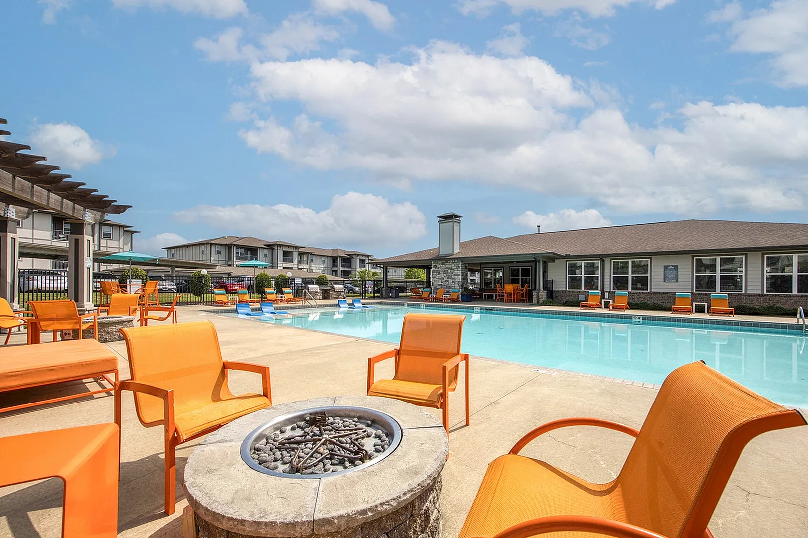 Luxurious apartment community featuring a stunning outdoor pool area with vibrant orange seating and a fire pit, perfect for relaxation under a bright blue sky.