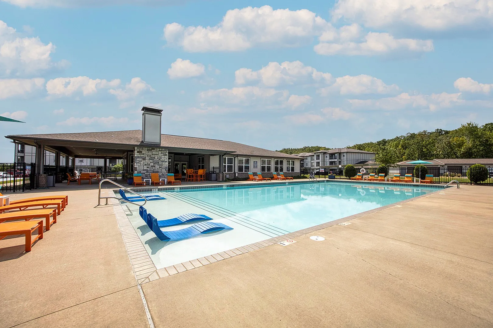 Luxurious outdoor pool area with comfortable seating, modern clubhouse, and vibrant landscape under a clear blue sky.